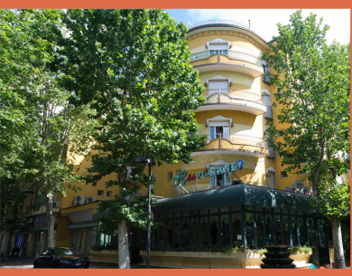 Edificio giallo con balconi e alberi verdi davanti.